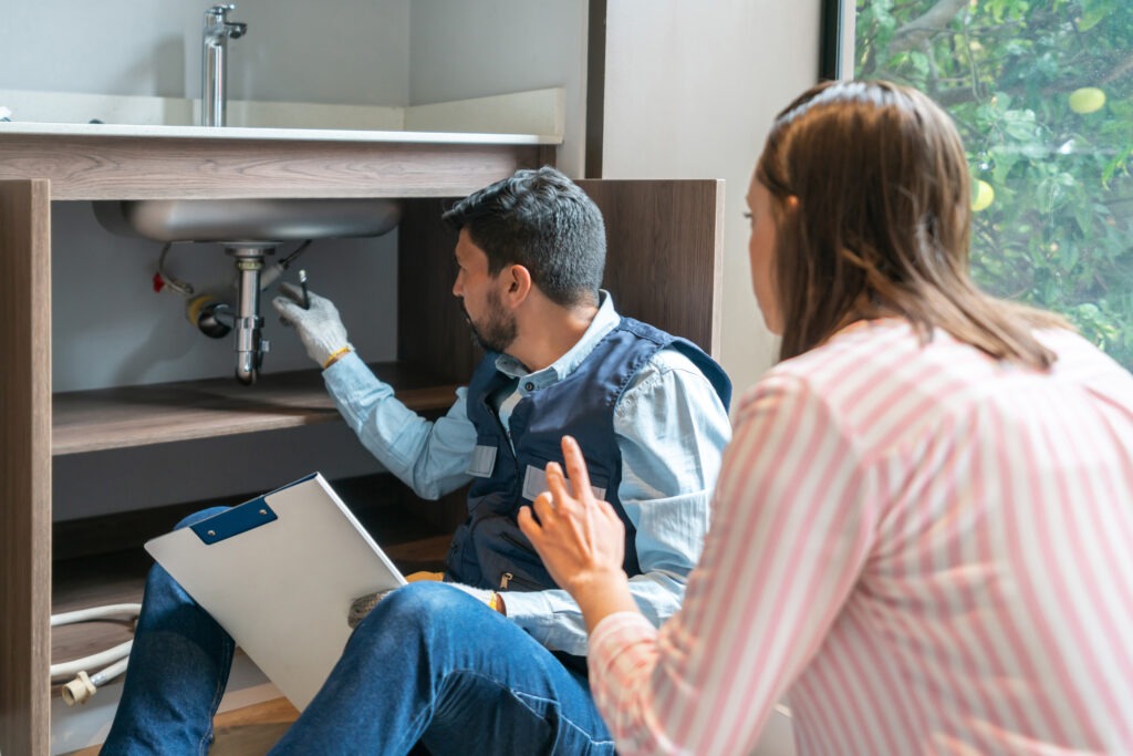 A plumber is shown inspecting a sink with a homeowner