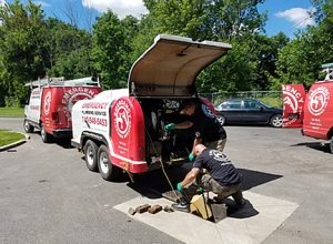 Two plumbers work on equipment inside a trailer.