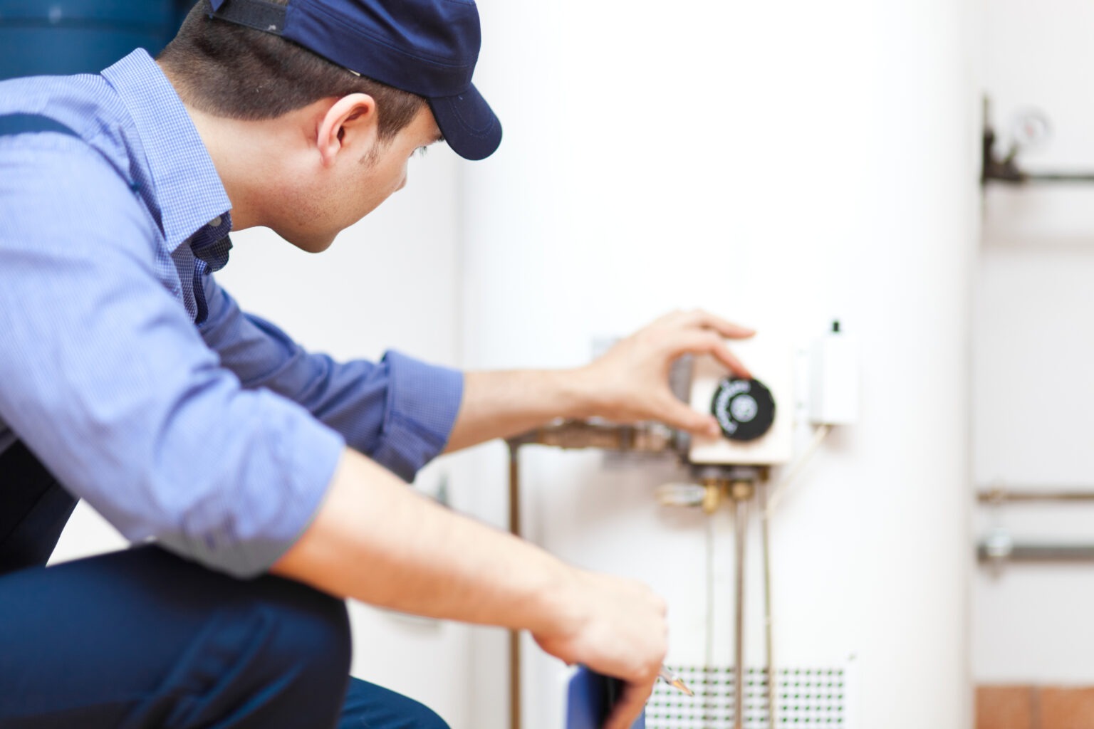 A service technician adjusts the temperature gauge of a white water heater.