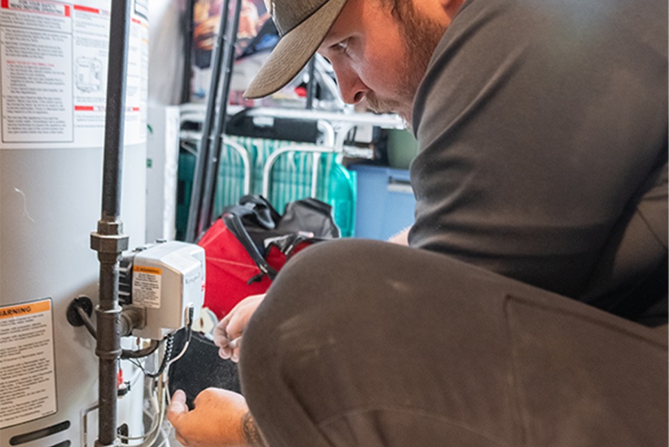 Man in gray shirt repairing a water heater.