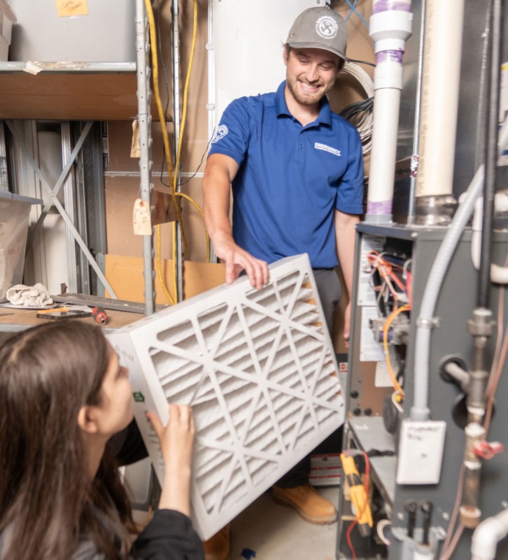 Two technicians are seen installing a new air filter in an HVAC unit.