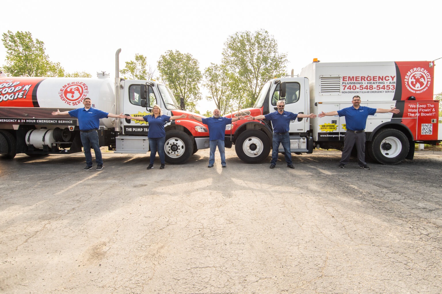 Five staff members stand arm-in-arm in front of company vehicles with text: &quot;Emergency Plumbing Heating Air - We Keep The Flowin' &amp; The Air Blowin'!&quot; and &quot;Scoop N Doogie Septic Service&quot;.