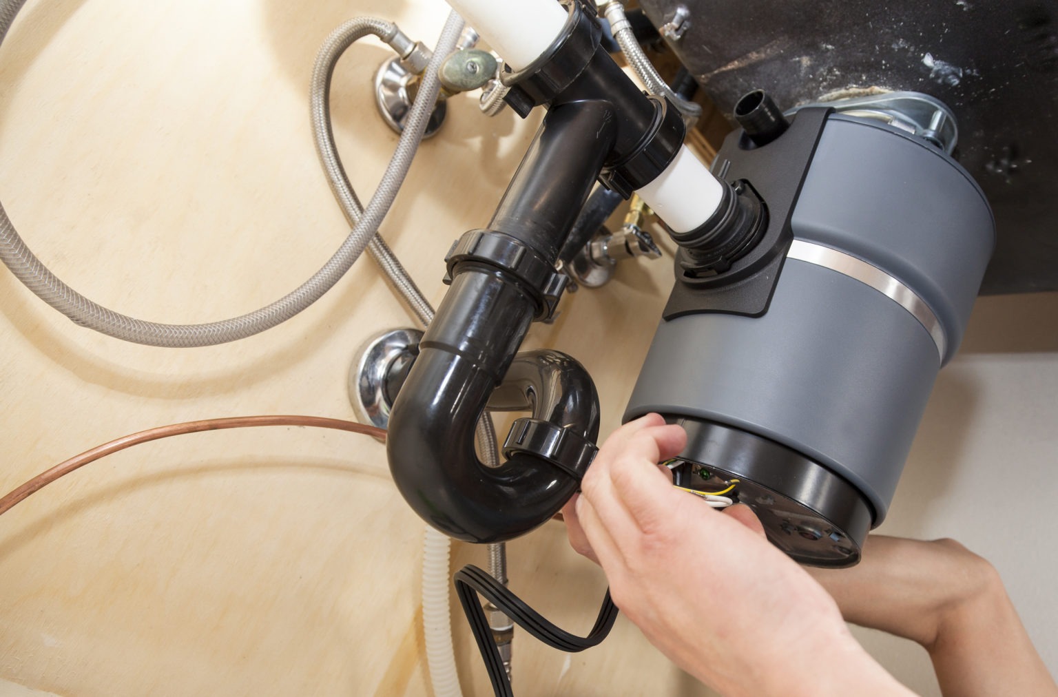 A plumber expertly connects a garbage disposal unit to sink plumbing.