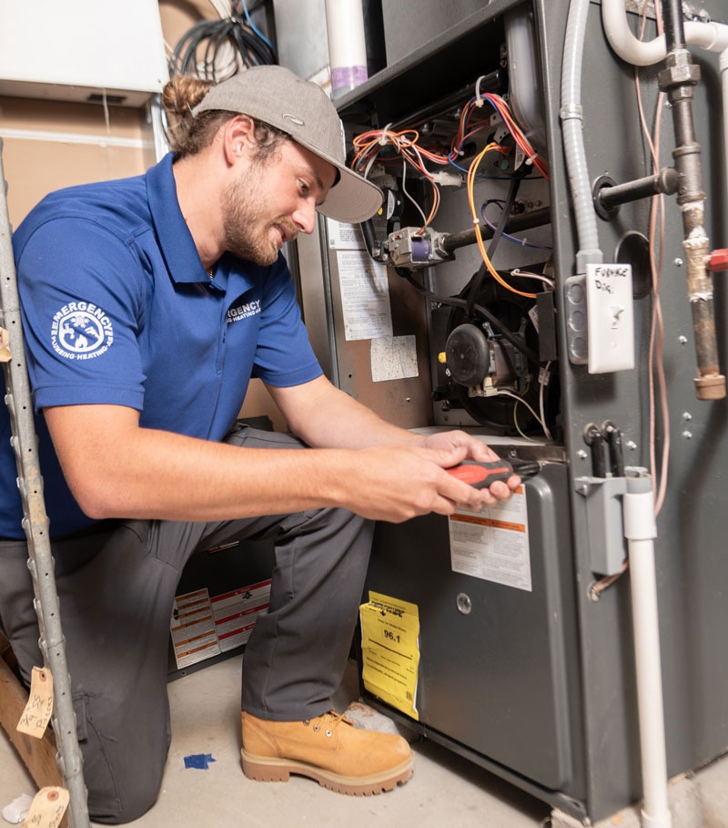 An HVAC technician kneels, inspecting a furnace.