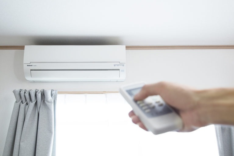 A hand points a remote at a wall-mounted air conditioning unit.