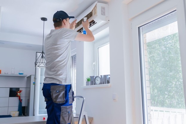 An HVAC technician repairs a ductless mini-split air conditioner inside a residential home.