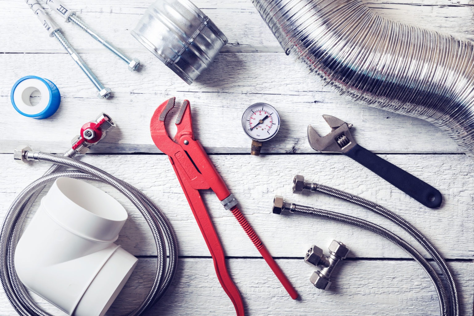 An overhead shot shows various plumbing and HVAC tools on a white wooden surface.