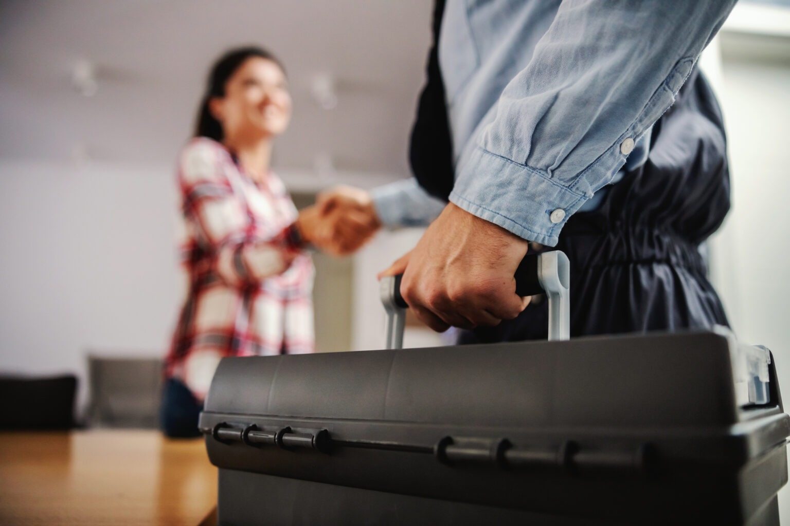 HVAC technician with toolbox shaking hands with smiling customer in their home.