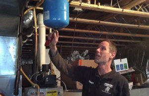 A plumber inspecting a blue expansion tank attached to plumbing and a furnace