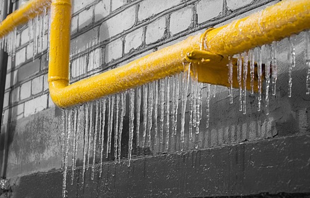 A horizontal yellow gas pipe with icicles runs along a brick wall