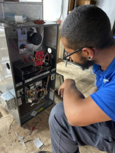 A technician kneels while inspecting the interior of an open furnace